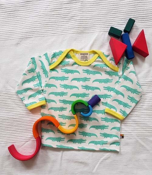 Tiere legen mit Holzspielzeug: Schlange aus Regenbogen von Grimms und Schmetterling mit Bauklötzen neben einem Shirt mit Krokodilen von Loud + Proud