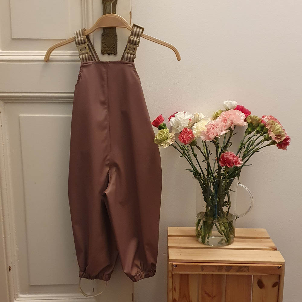 Regenhose mit Latz von Wheat an einem Bügel neben einer Vase mit Blumen