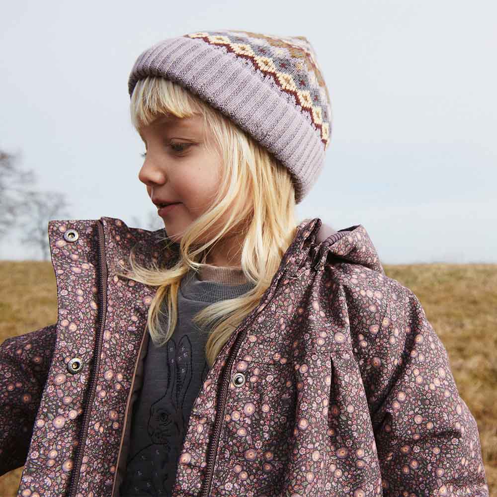 Ein Kind in einer Winterjacke von Wheat steht auf einer Wiese