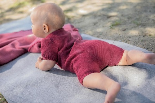 Baby liegt auf einer Decke und ist bekleidet mit einem Strampler aus Wolle von Disana