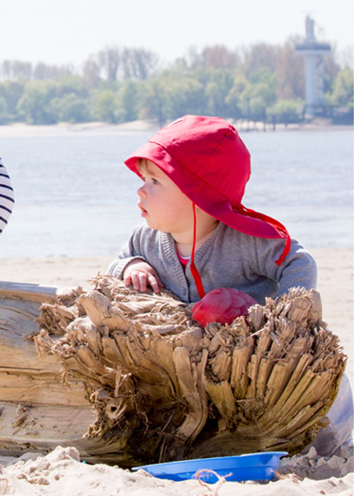 Baby mit rotem Pickapooh Sonnenhut am Meer