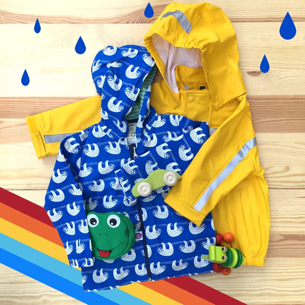 Eine gelbe Regenjacke von BMS umarmt eine blaue, wassabweisende Jacke mit Faultier Muster von Loud + Proud. Dazu kombiniert eine Geldbörse von Affenzahn, ein grünes Holzauto von Grimms Holzspielzeug sowie ein Klapperkroko Rassel Spielzeug von Selecta. Umrahmt ist das Bild von einen Regenbogen und Regentropfen.